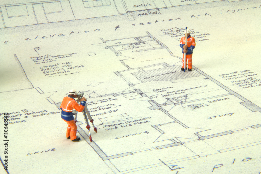 Two miniature figures in high-vis uniform with a theodolite survey a house blueprint