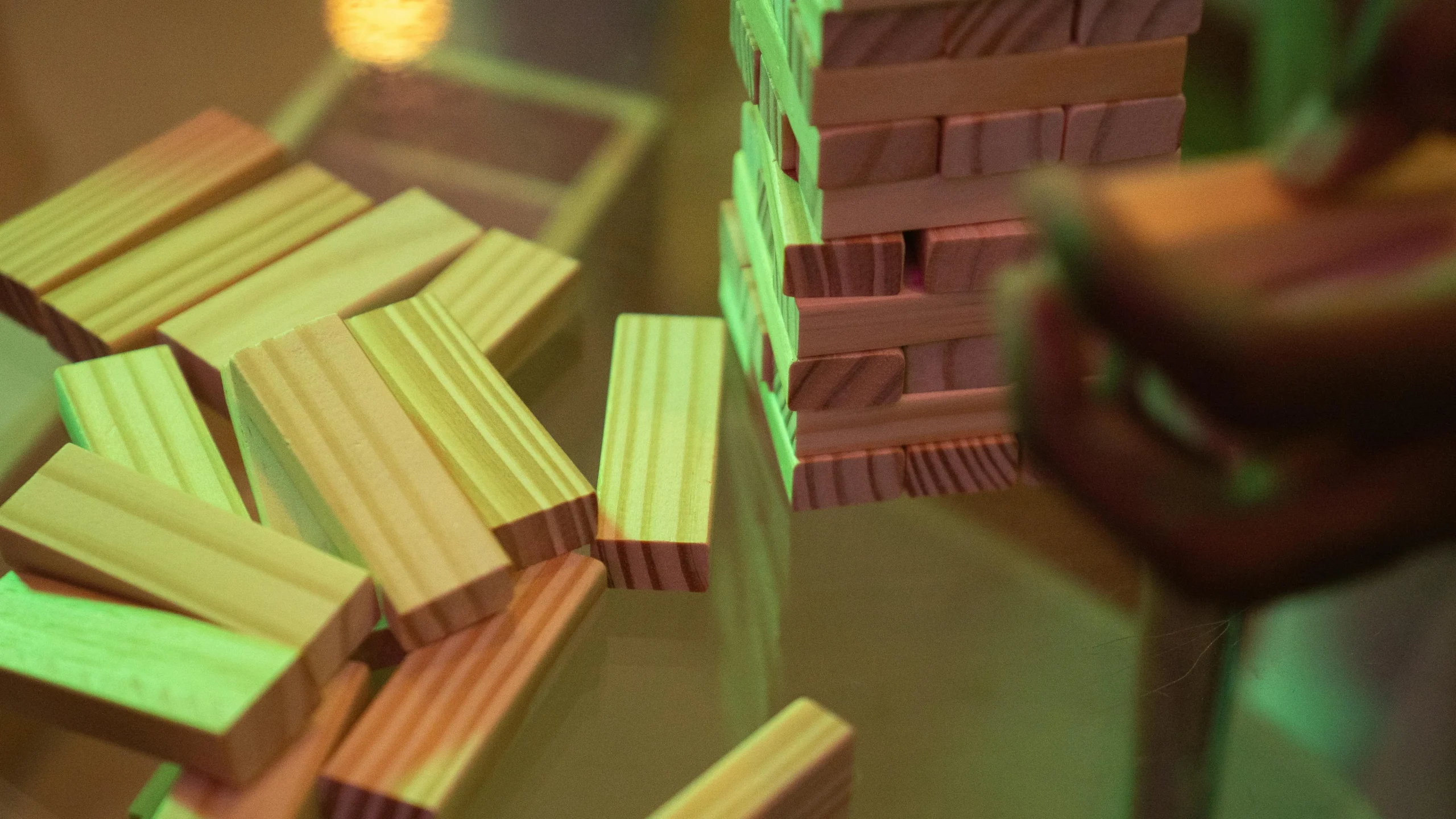 A stack of Jenga blocks beside scattered pieces on a glass table with dramatic lighting.