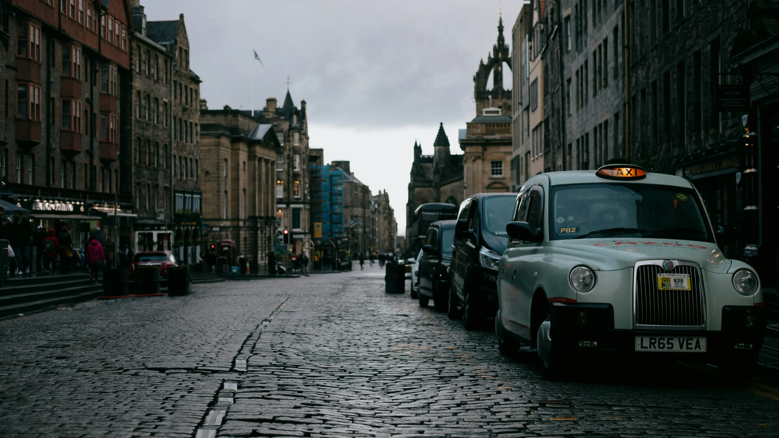 Street with parked cars between aged multistage building exteriors under gray sky in city