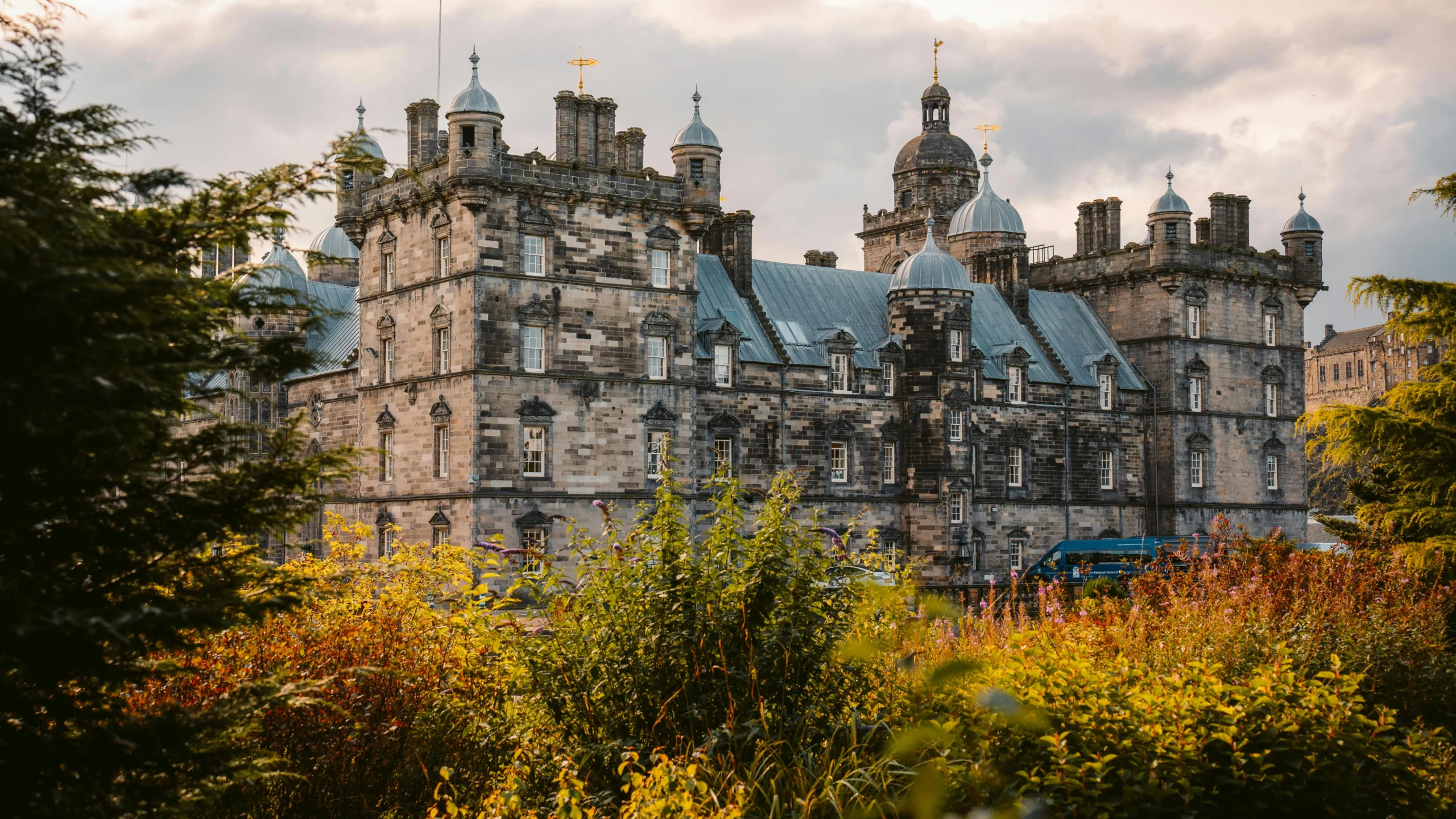 Stunning view of a historic Scottish castle framed by vibrant autumn foliage, under a cloudy sky.
